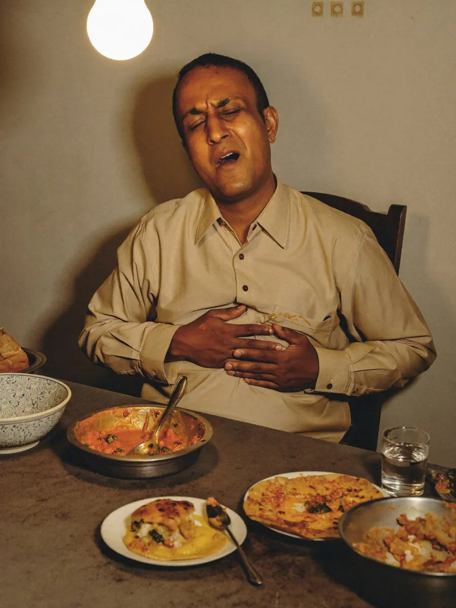 A man sitting back from the table after a heavy meal, hand resting on his stomach