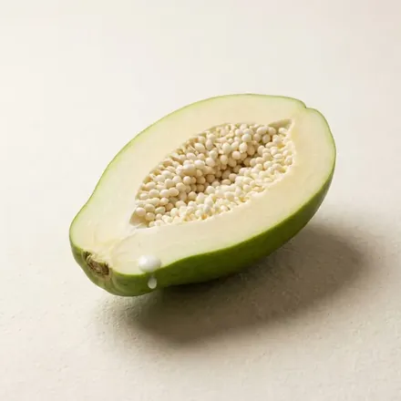 A green unripe papaya cut in half, showing pale flesh and white seeds