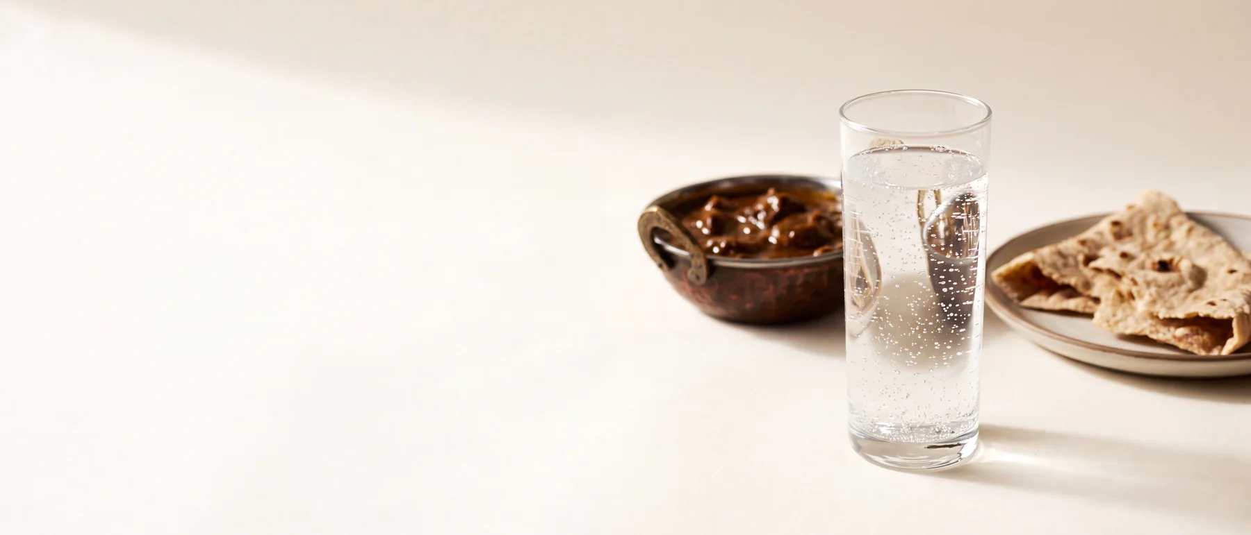 A glass of water full of rising bubbles beside the remains of a rich meal, on plain cream paper